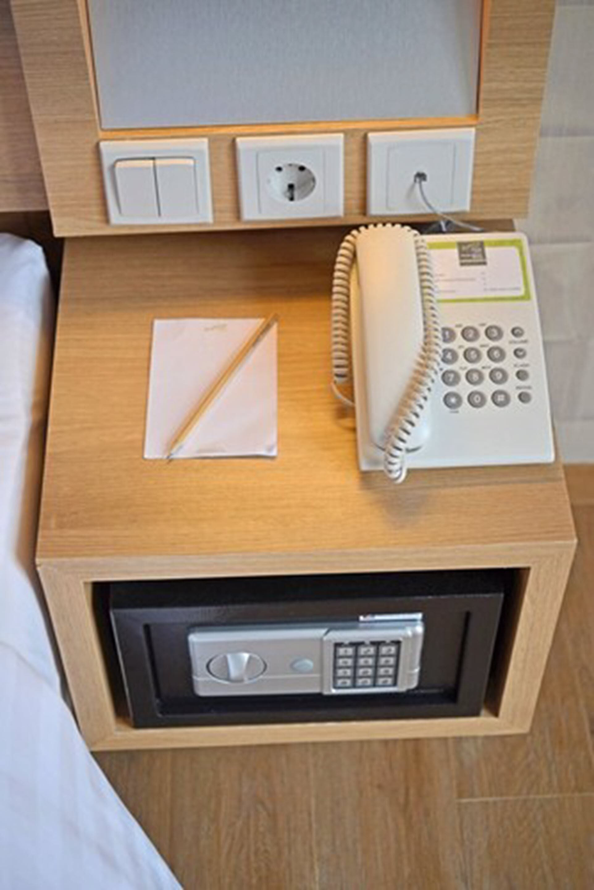Una mesita de noche de madera con un teléfono, un bloc de notas y una caja fuerte.