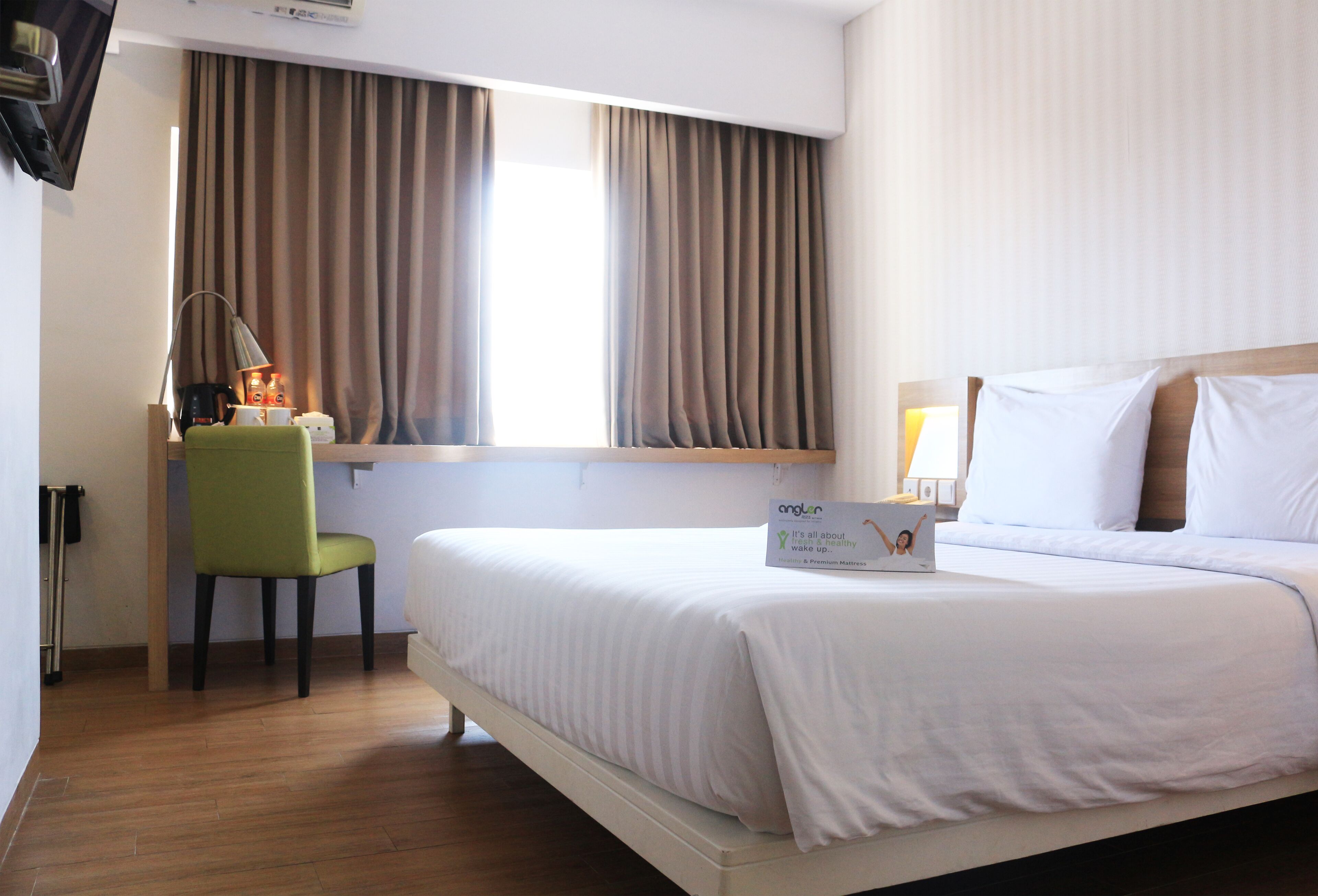 A hotel room with a bed, a desk with a lamp, a chair, and a window with curtains.