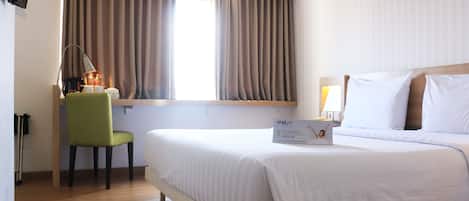 Habitación de hotel con cama, escritorio con lámpara, silla y ventana con cortinas.