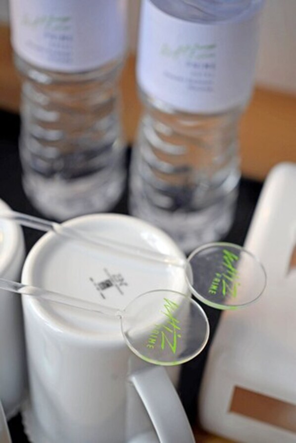 A tray with multiple clear water bottles and white mugs with green labels.