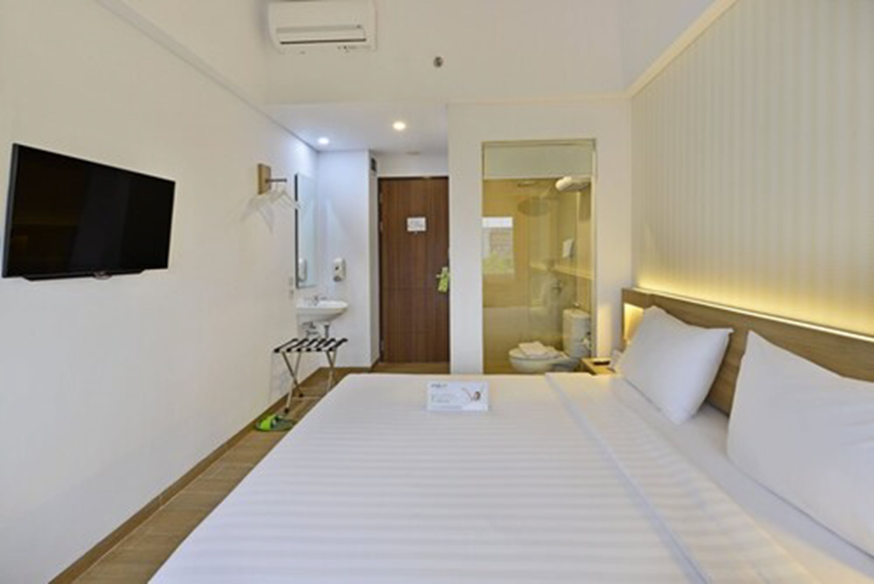 Quarto de hotel com cama, televisão fixada na parede, pia e espelho.