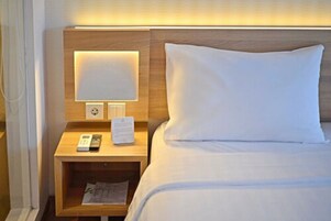 Habitación de hotel con cabecera de madera, mesita de noche con lámpara, control remoto y bloc de notas.