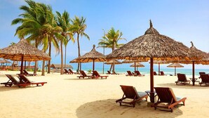 A beach with thatched umbrellas and wooden lounge chairs. - Ocean Villas Beach Resort (Da Nang)