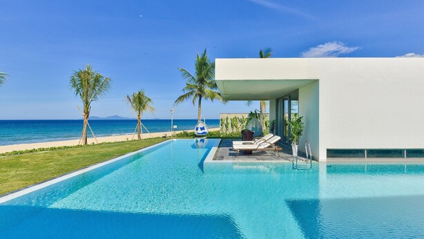 A modern pool area with clear blue water, lounge chairs, and a view of the ocean. - Ocean Villas Beach Resort (Da Nang)