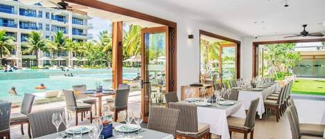 A restaurant with tables set for dining, overlooking a pool area with guests.