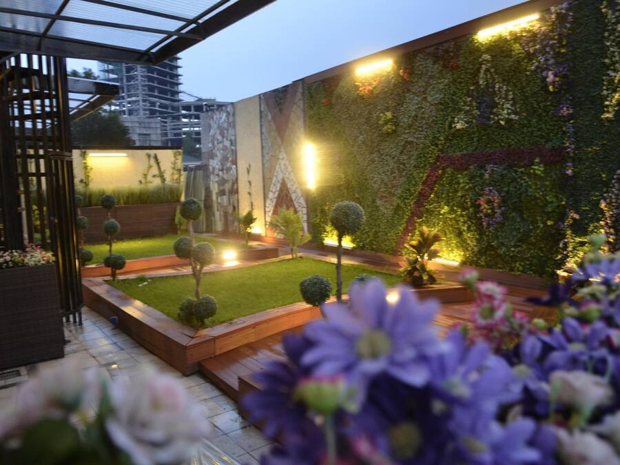 A modern outdoor garden with a glass structure, neatly trimmed grass, and a variety of plants and flowers.