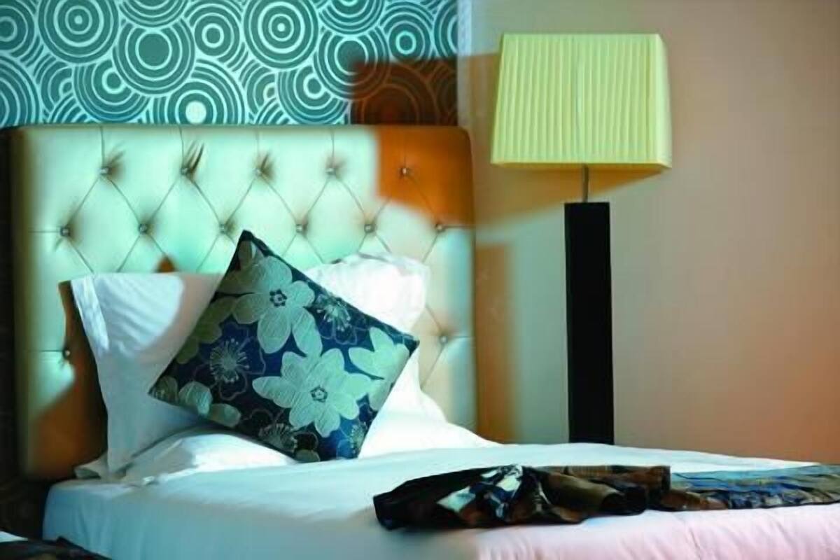 A bed with a tufted headboard, a floral pillow, and a striped throw blanket.