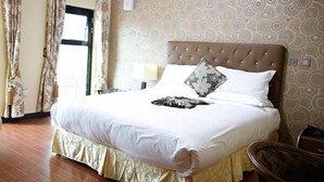 Una cama bien hecha con un cojín estampado, una lámpara de noche y una ventana con cortinas.