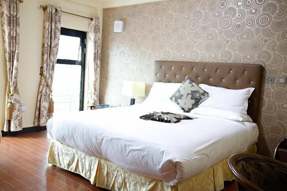 A neatly made bed with a patterned pillow, a bedside lamp, and a window with curtains.