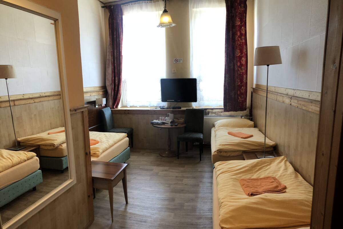 Een compacte hotelkamer met twee éénpersoonsbedden, een klein bureau met stoel, een televisie en een raam met gordijnen.