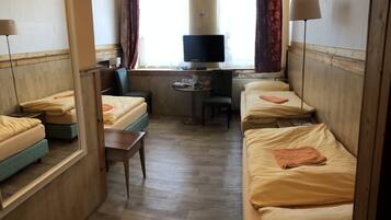 A compact hotel room with two single beds, a small desk with a chair, a television, and a window with curtains.