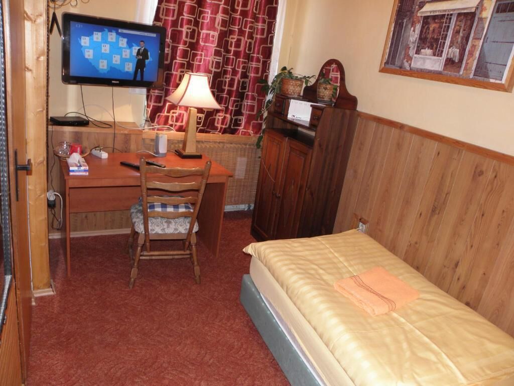 A small, cozy room with a wooden desk, a chair, a bed, a television, and a lamp.