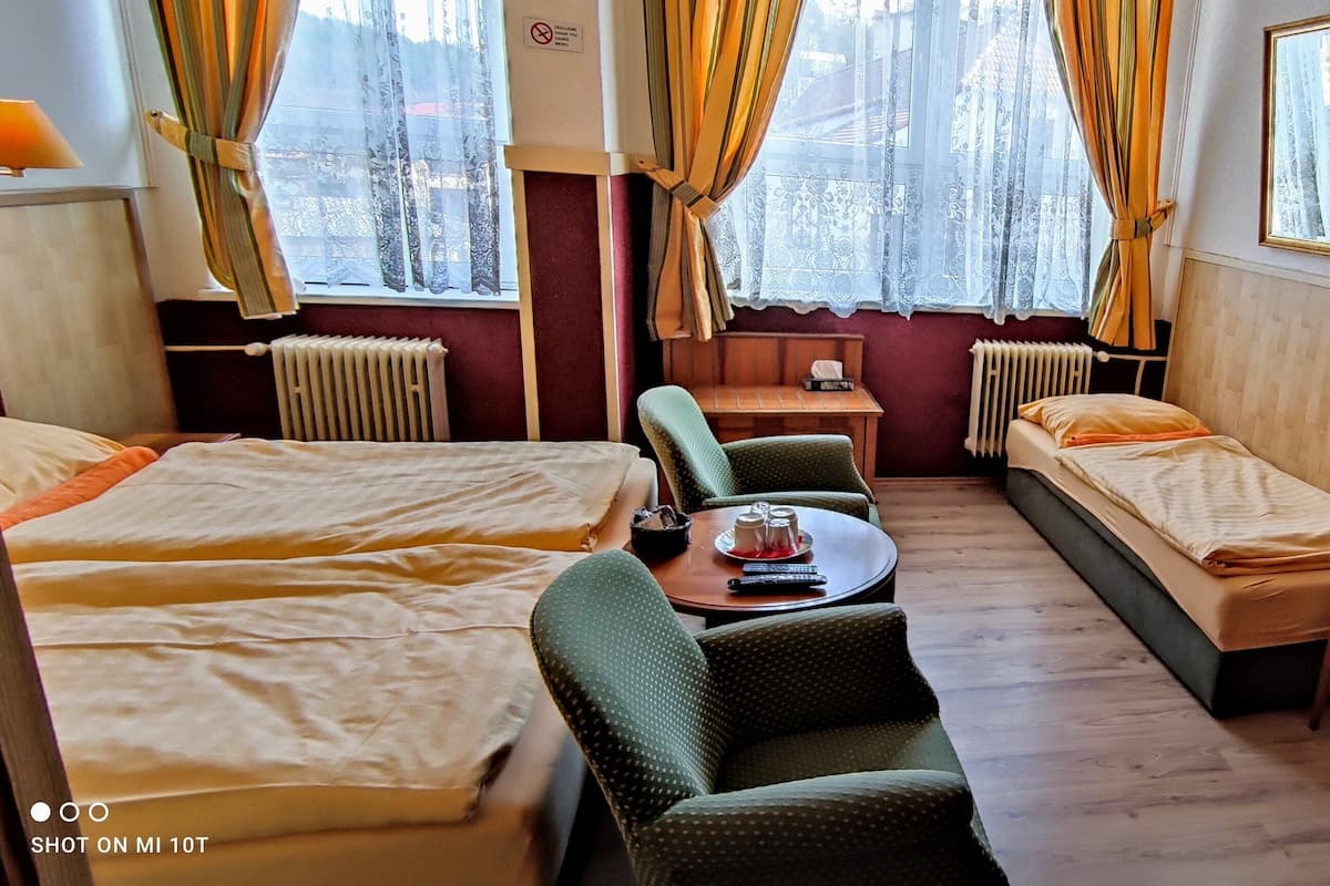 Een hotelkamer met twee eenpersoonsbedden, een slaapbank, een tafeltje met een afstandsbediening, een televisie en een raam met gordijnen.
