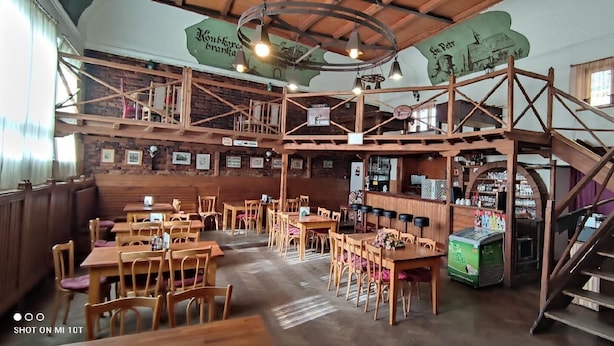 A rustic interior with wooden tables and chairs, a staircase, and a bar area. - Hotel U Branky (Stribro)