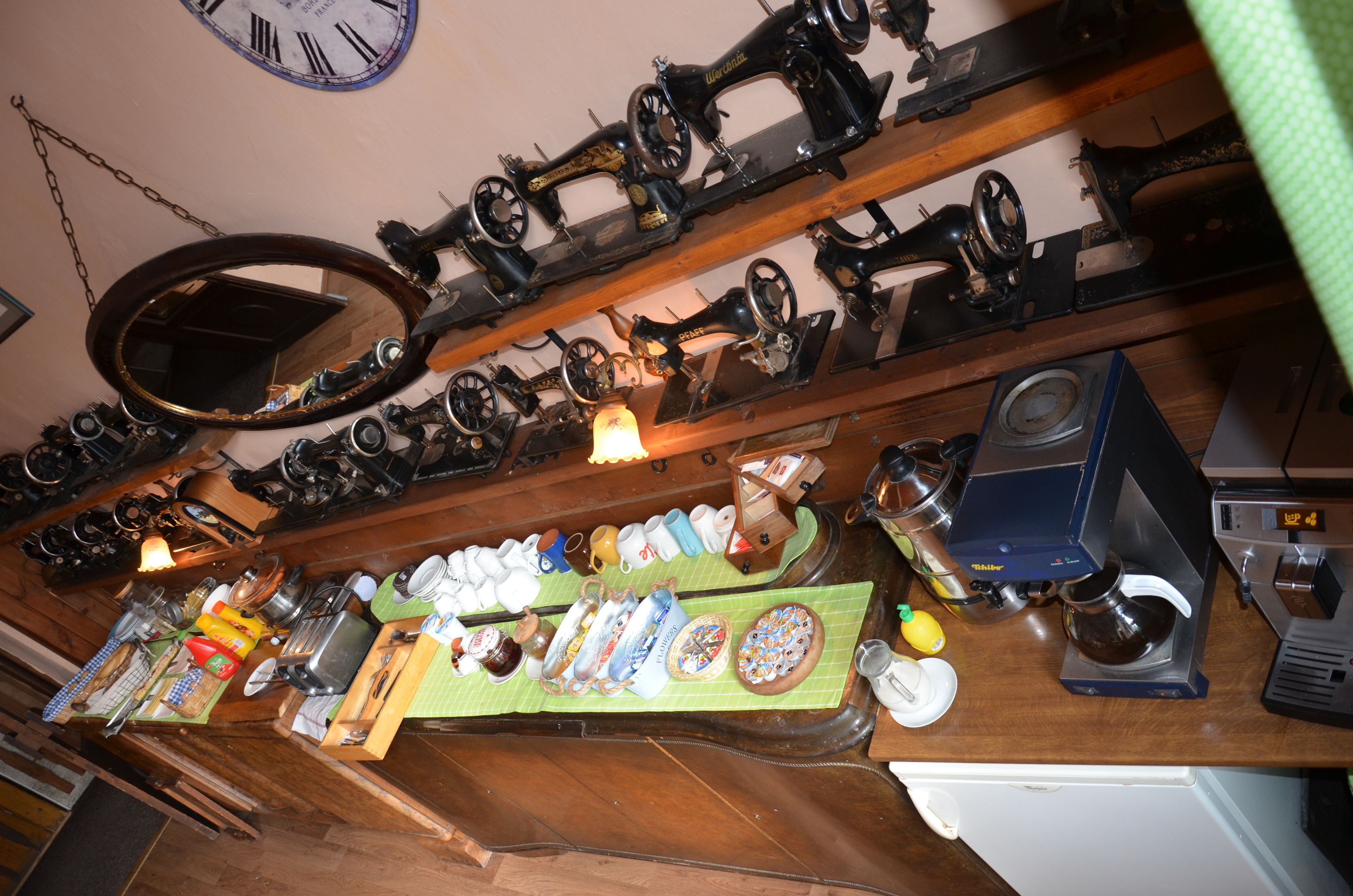 A kitchen with vintage sewing machines on shelves, a clock on the wall, and a variety of kitchen utensils and appliances on the counter.