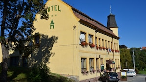 A yellow building with a sign reading "HOTEL" and a tower with a spire. There are flower boxes on the windows and a car parked in front. - Hotel U Branky (Stribro)