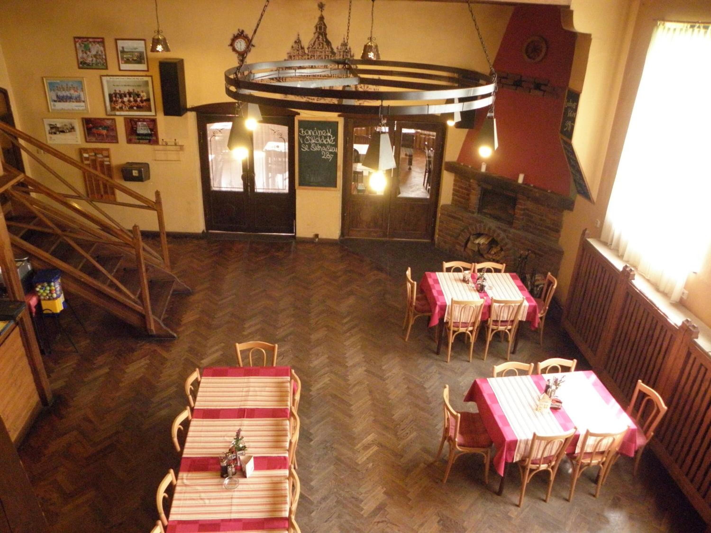 Un comedor con mesas y sillas de madera, un suelo con motivo de espiga y una escalera que lleva a un nivel superior.