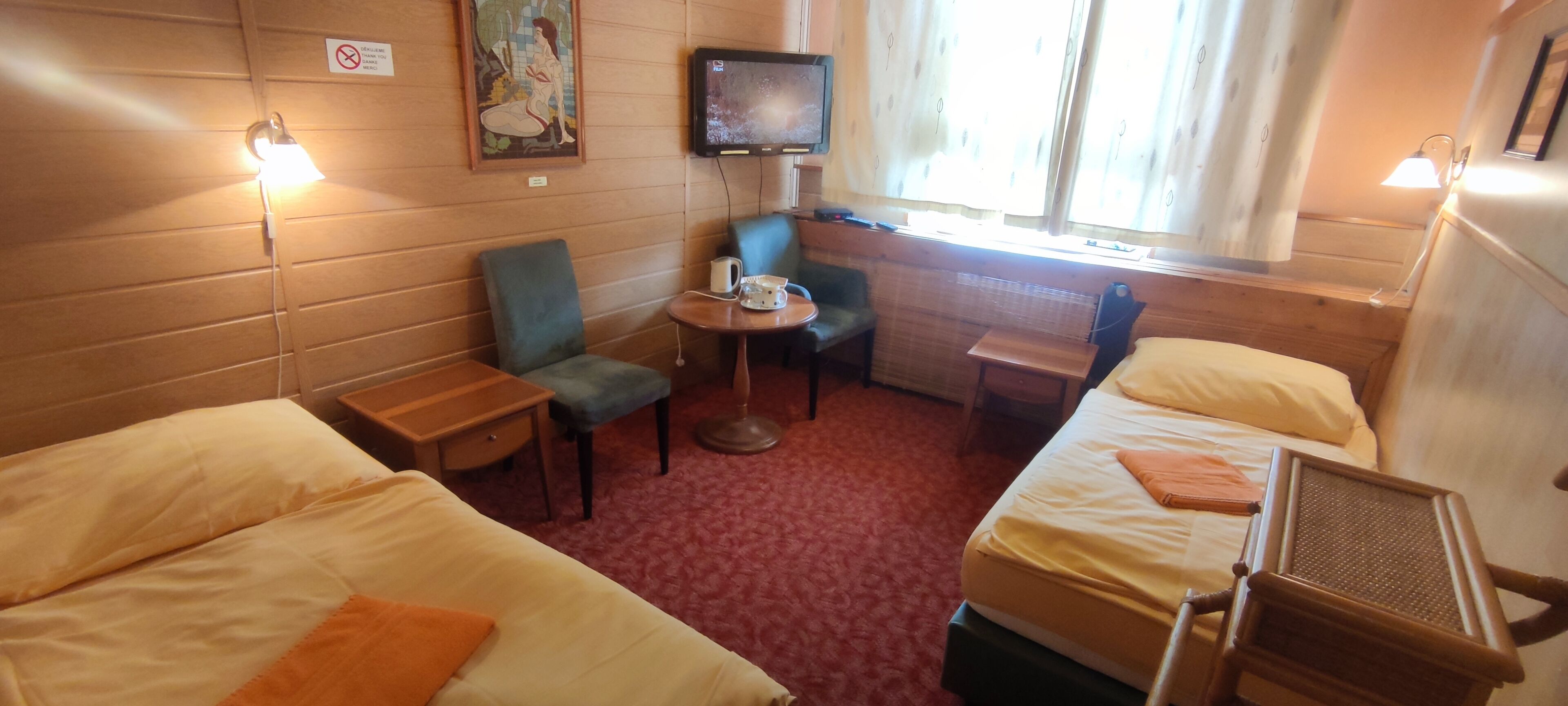 A hotel room with two single beds, a small table with a chair, a television, and a window with curtains.