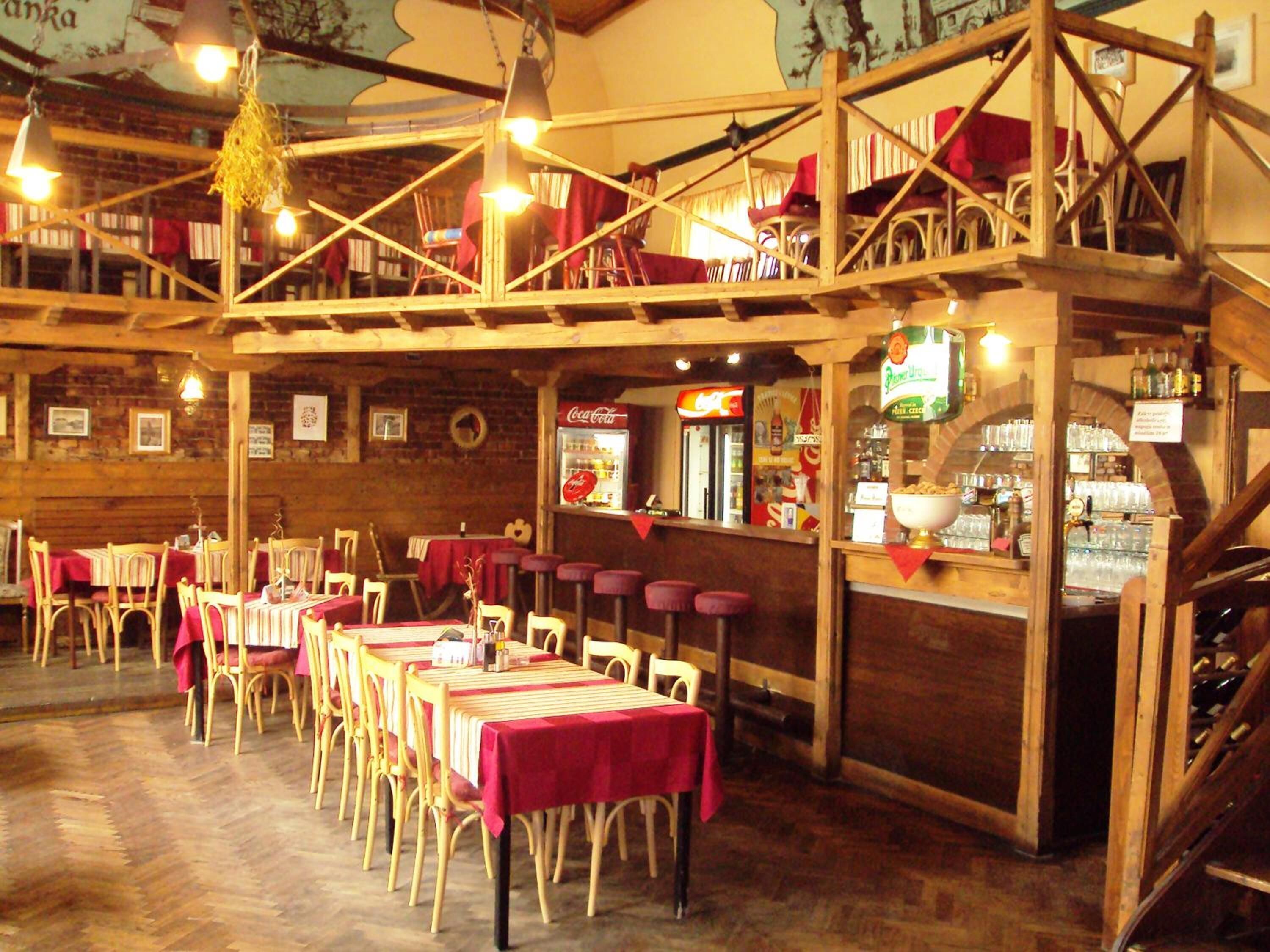 Un restaurante rústico con mesas y sillas de madera, una zona de bar y un refrigerador de Coca-Cola.