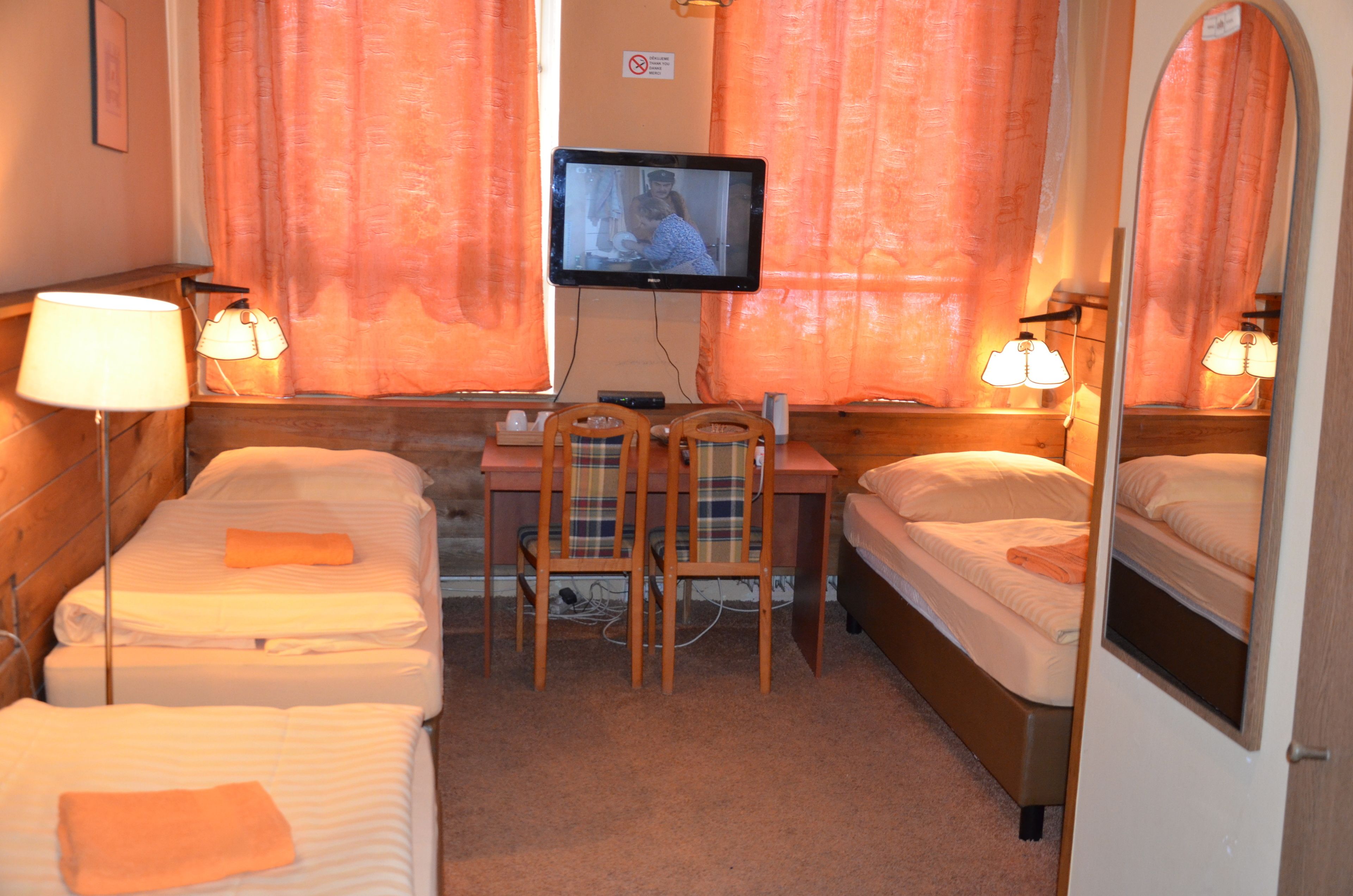 Quarto de hotel com duas camas, uma escrivaninha, uma cadeira, uma televisão e duas luminárias.