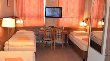 Quarto de hotel com duas camas, uma escrivaninha, uma cadeira, uma televisão e duas luminárias.