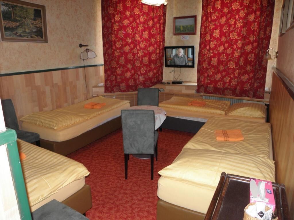 A hotel room with two beds, a chair, a television, and a red carpet.