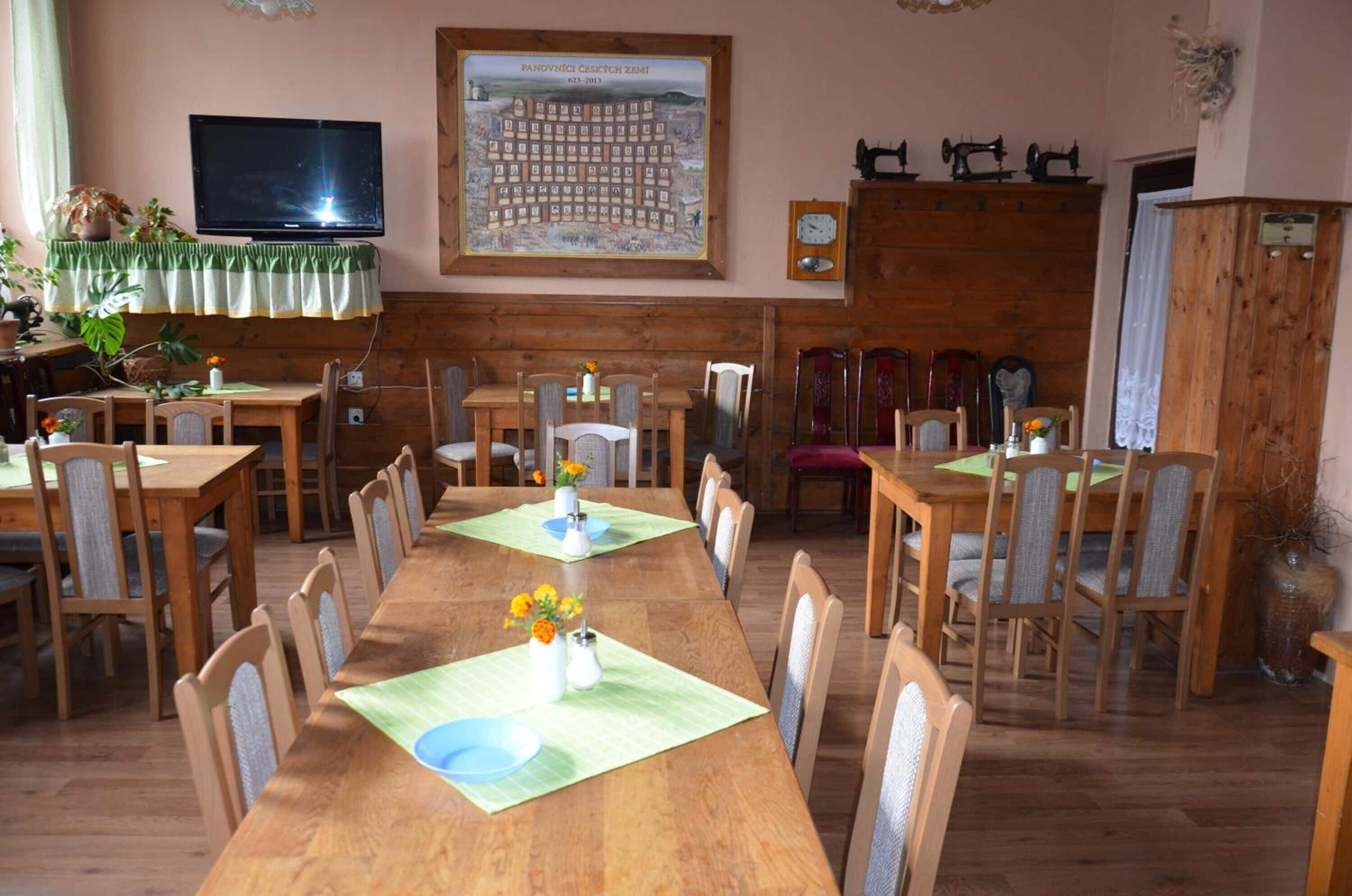 Un’area pranzo con diversi tavoli e sedie in legno, una televisione montata a parete e una mappa incorniciata sopra i tavoli.