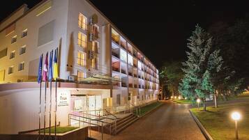 Un hotel de varios pisos con un diseño moderno, que presenta una escalera central que conduce a la entrada y un exterior bien iluminado.