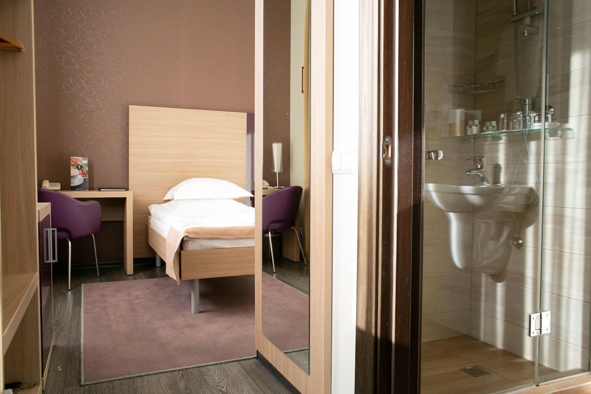 A hotel room with a bed, a desk, a chair, and a shower area.