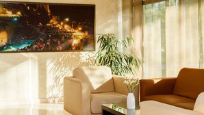 A modern living room with a beige sofa, a coffee table, and a large painting of a cityscape. - Puscha Congress Hotel (Kyiv)