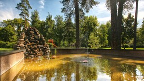 A tranquil pond with a stone structure and a playground in the background. - Puscha Congress Hotel (Kyiv)