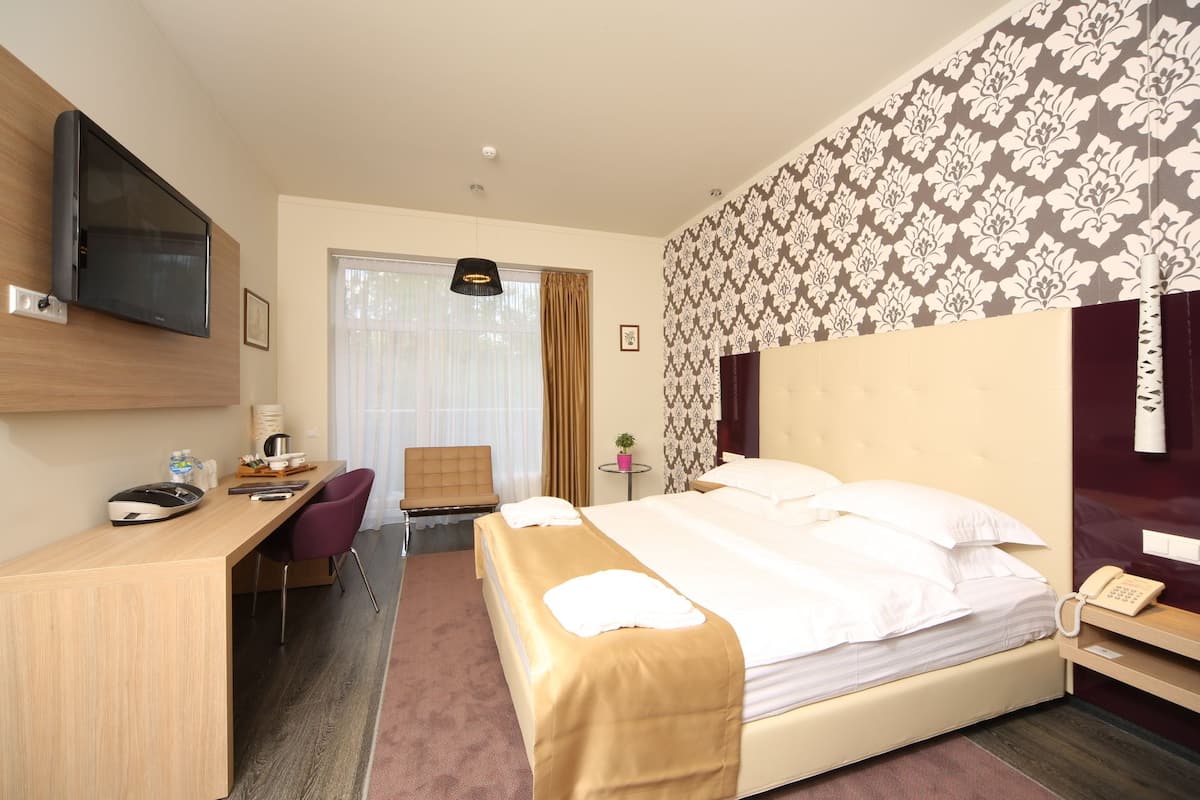 A hotel room with a bed, desk, chair, and a television mounted on the wall.