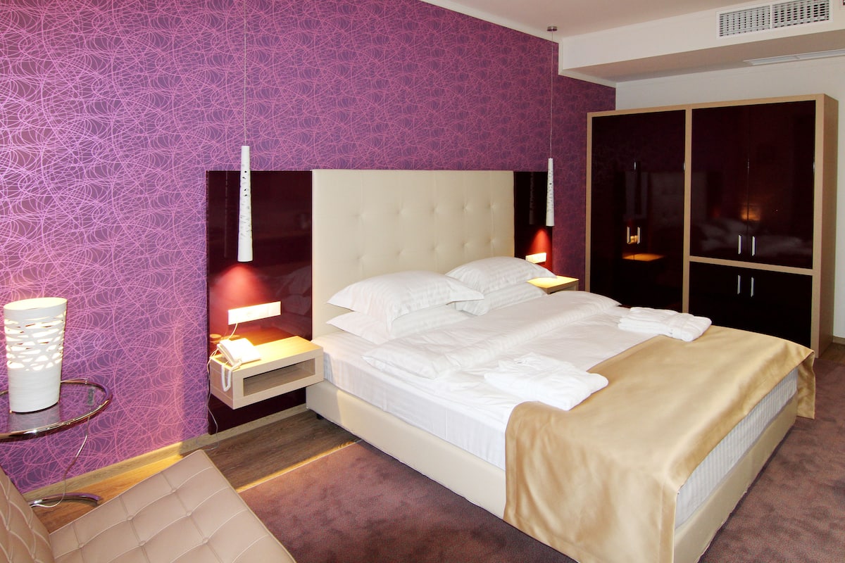 A hotel room with a large bed, a wardrobe, and a bedside table with a lamp.