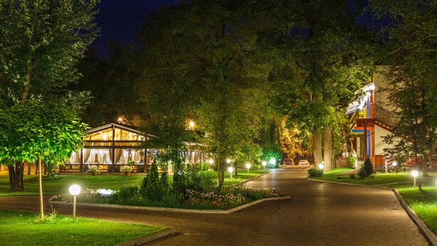 A well-lit, tree-lined street leading to a building with a glass facade and outdoor seating area. - Puscha Congress Hotel (Kyiv)