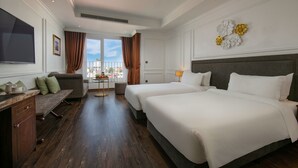 A hotel room with two beds, a desk, a chair, a TV, and a view of the city. - Hanoi Allure Hotel (Hanoi)