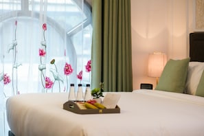 A hotel room with a bed, a tray with toiletries, a clock, and a window with floral curtains.