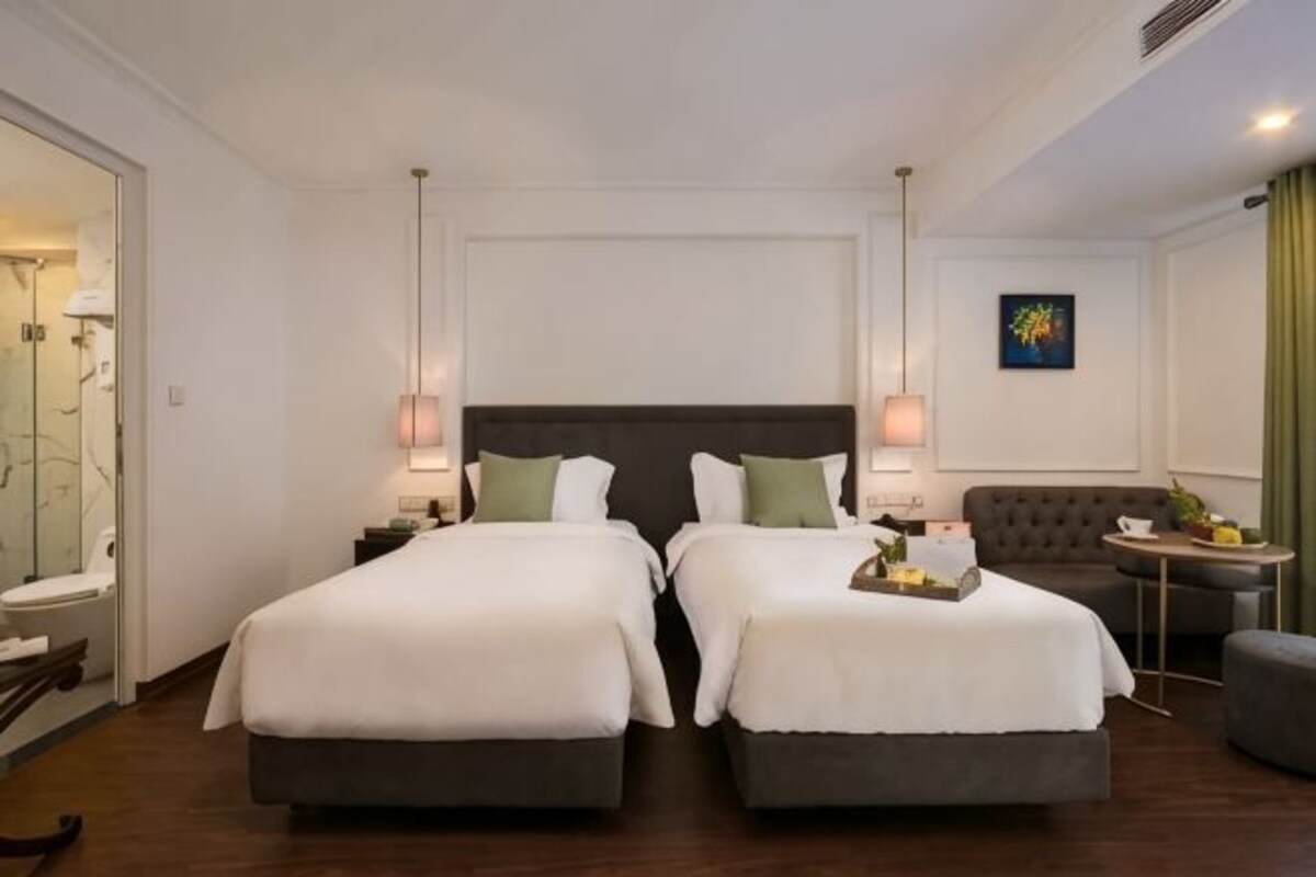 A hotel room with two beds, a sofa, a small table, and a mirror.