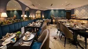 A restaurant with a long counter, multiple tables, and booths, featuring a modern interior design with blue and grey tones. - Hanoi Allure Hotel (Hanoi)
