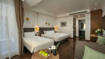 A hotel room with two beds, a round table with apples and flowers, and a sofa.
