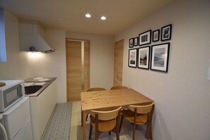 A compact kitchen with a microwave, sink, and wooden cabinets. There is a dining table with four chairs and a small rug.