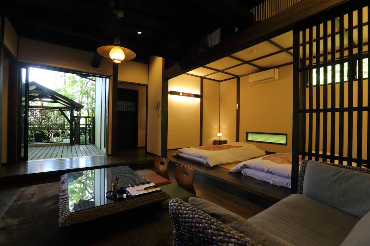 A traditional Japanese-style room with tatami flooring, a low table with a tray, a sofa, and a bed with a futon.