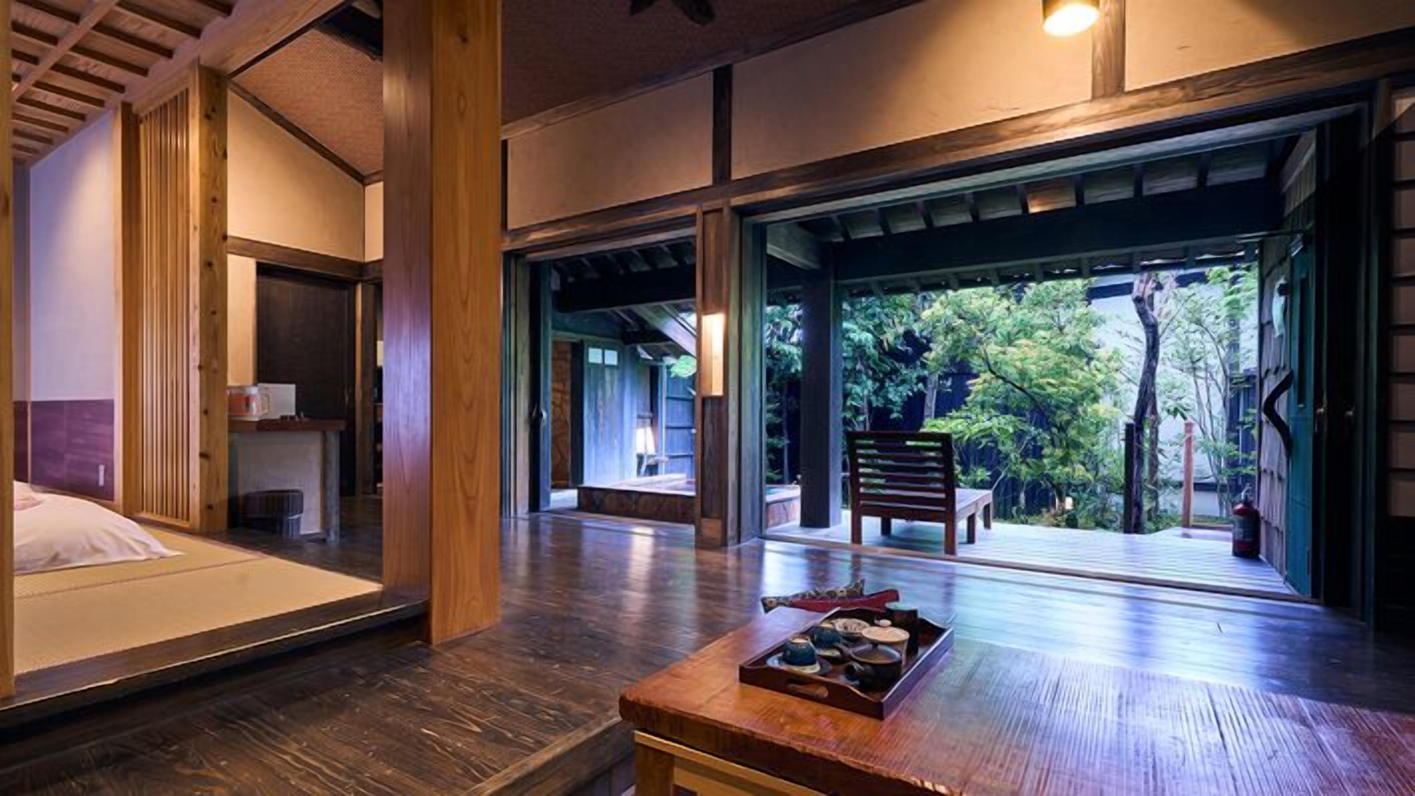 A traditional Japanese-style room with tatami flooring, a low wooden table with tea set, and a view of a garden through sliding doors.