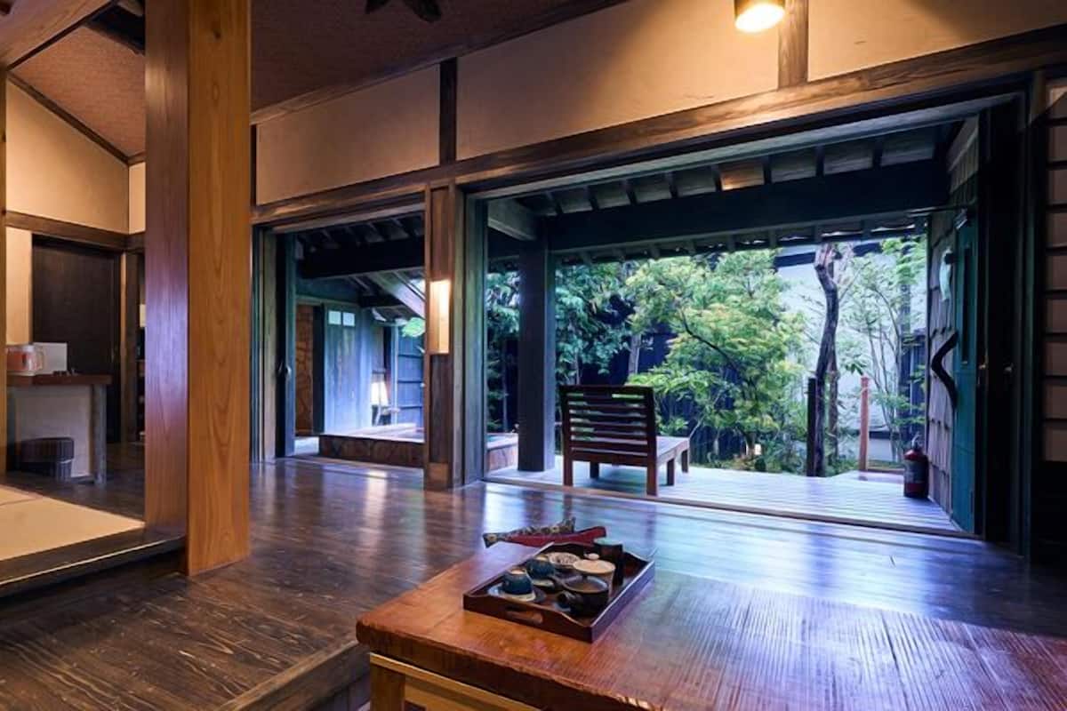 A traditional Japanese-style room with tatami flooring, a low wooden table with tea set, and a view of a garden through sliding doors.