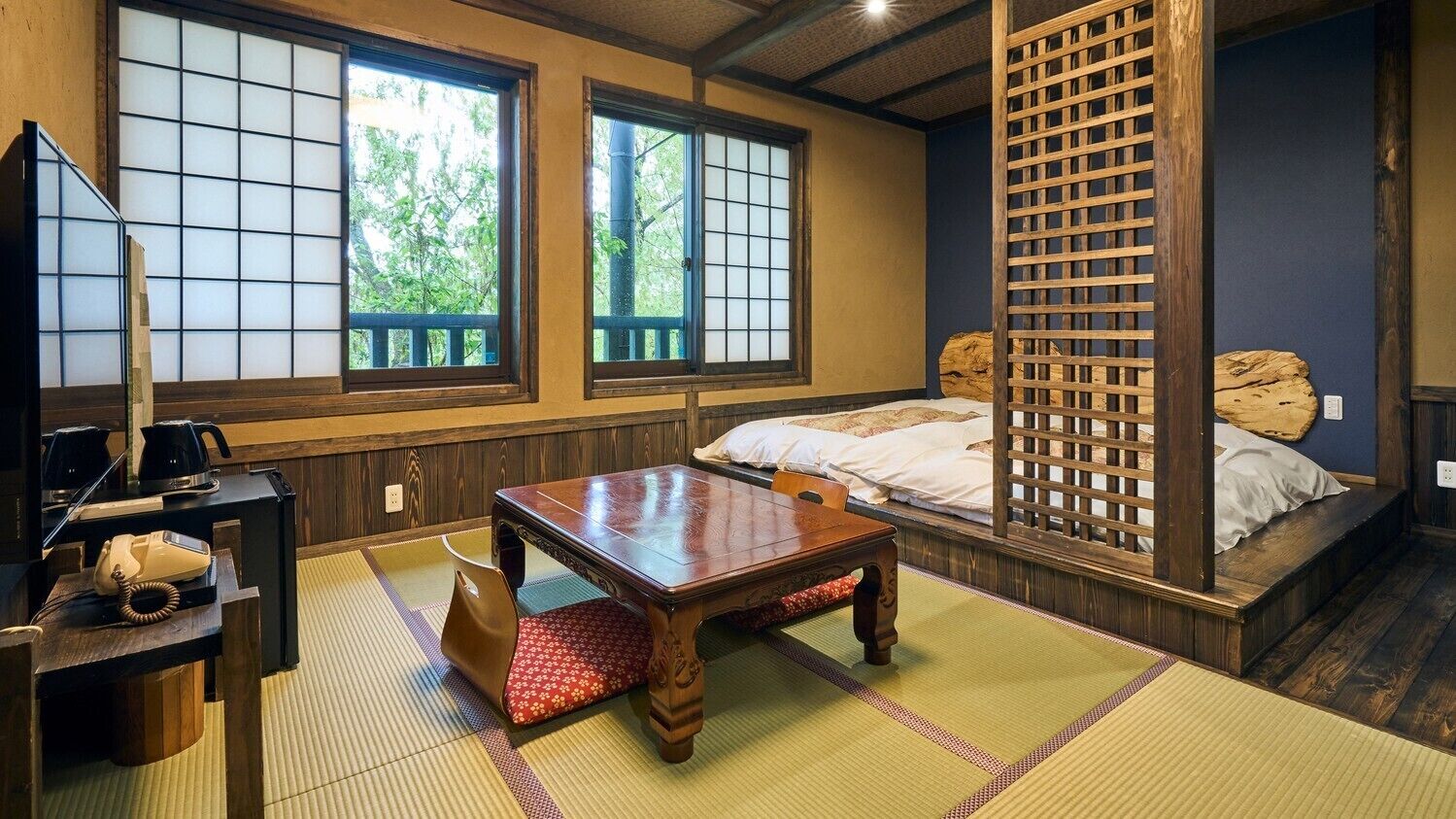 A traditional Japanese room with tatami flooring, a low wooden table, a bed with a wooden headboard, and sliding doors with a view of greenery outside.