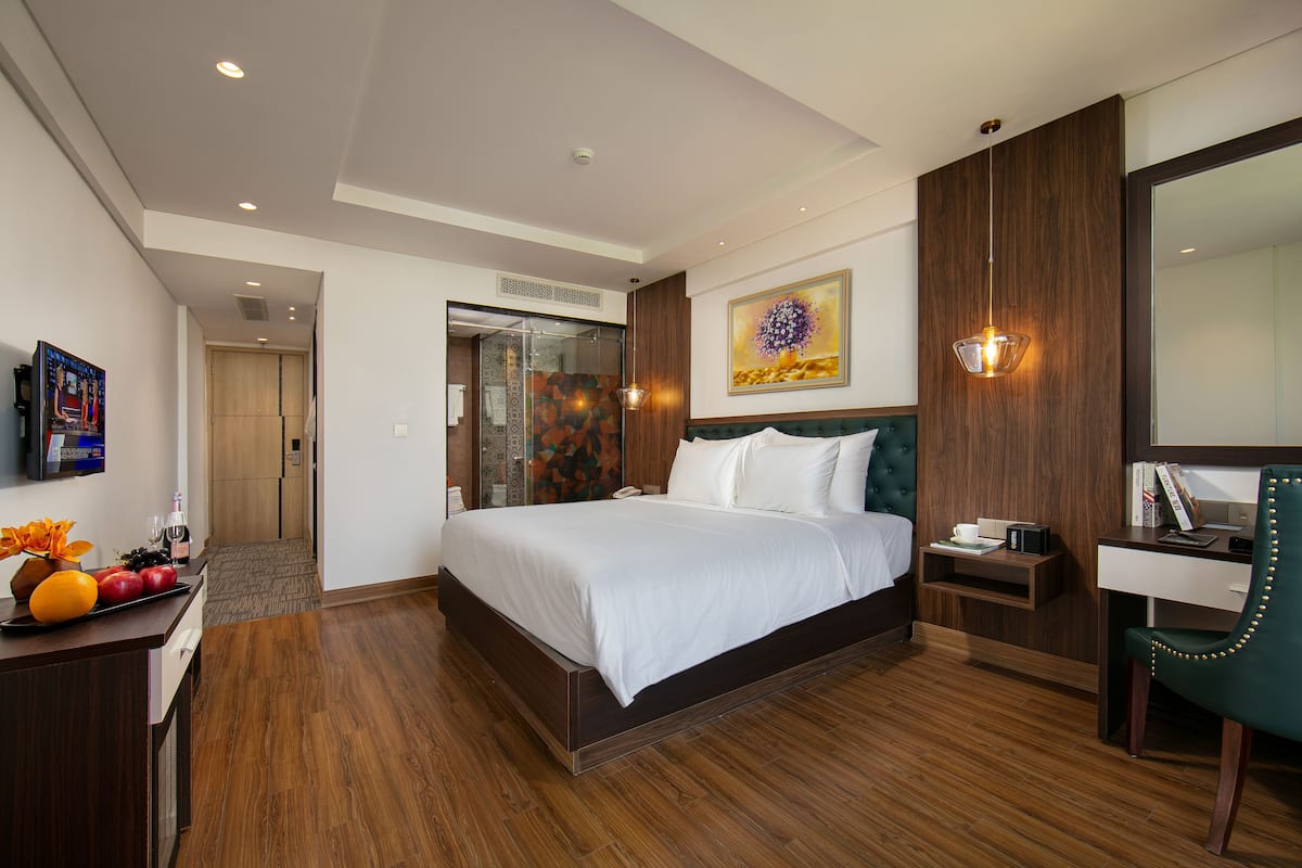 A modern hotel room with a large bed, a desk, a chair, a shower area, and a bathroom.