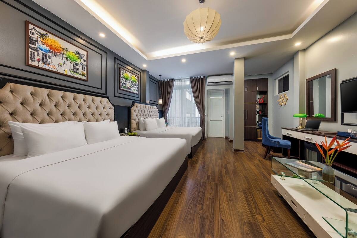 A hotel room with two beds, a desk, a chair, a TV, and artwork on the walls.