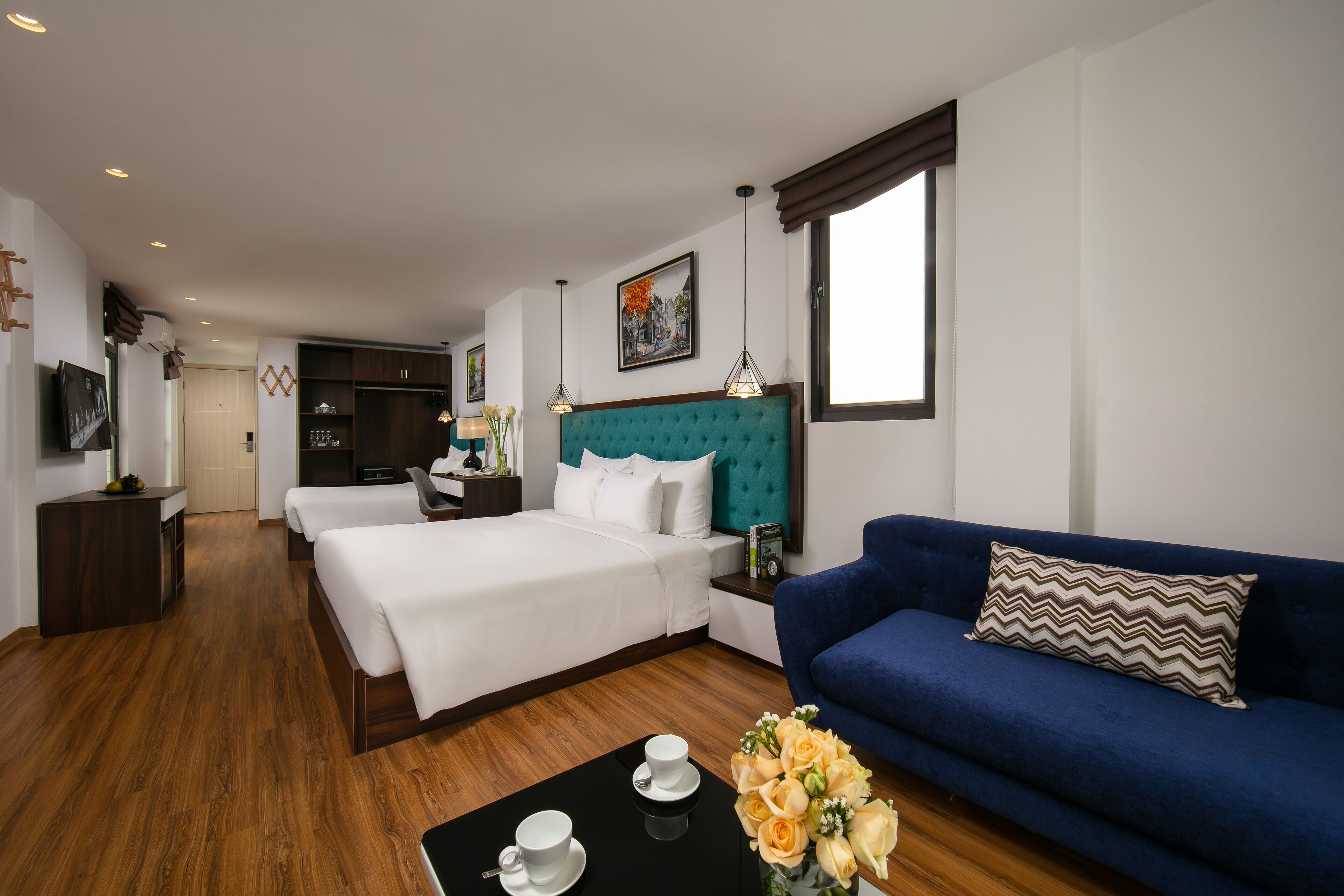 A hotel room with a large bed, a blue sofa, a coffee table with a vase of flowers, and a painting on the wall.