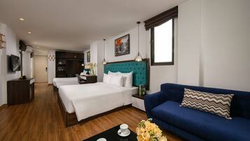A hotel room with a large bed, a blue sofa, a coffee table with a vase of flowers, and a painting on the wall.