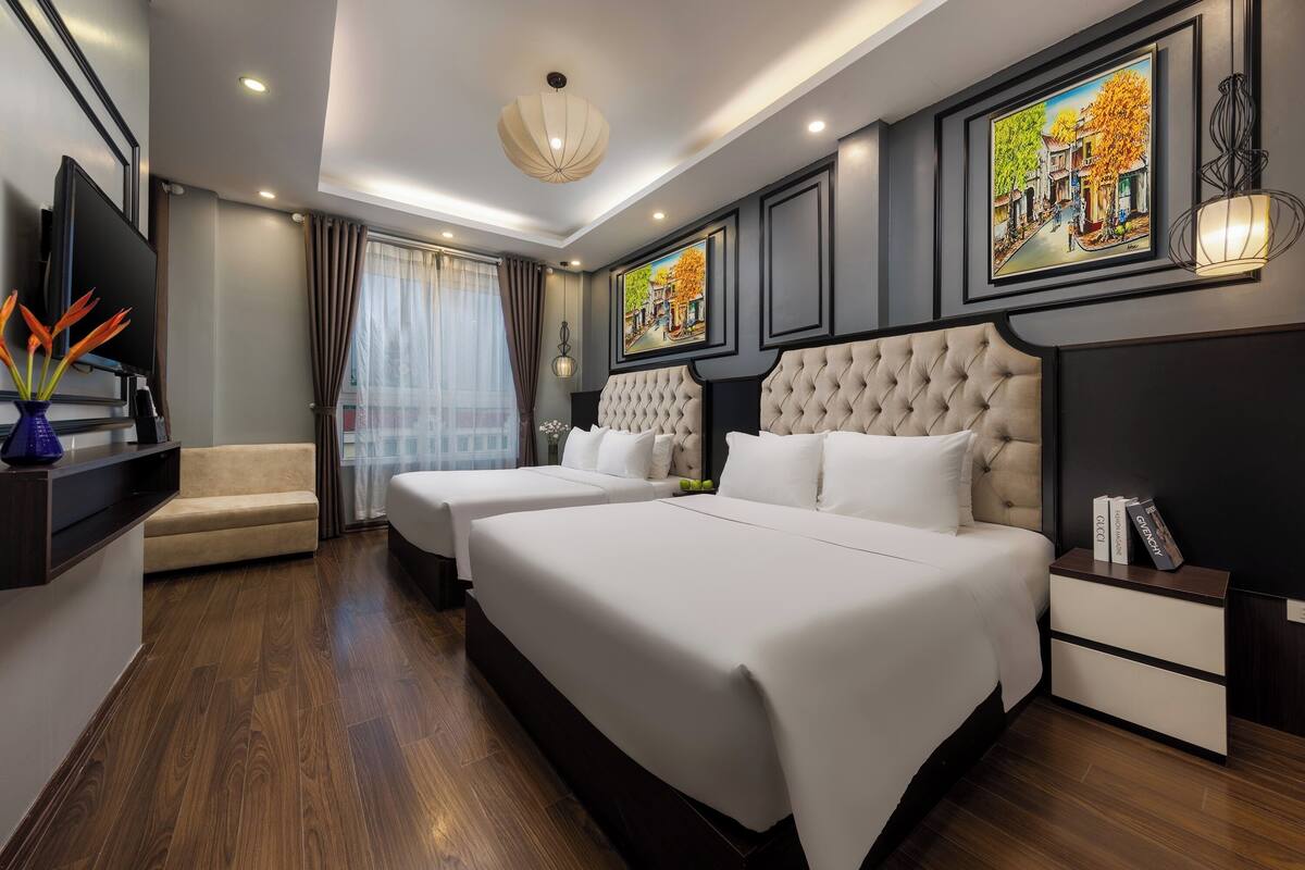 A hotel room with two beds, a TV, a sofa, and a painting on the wall.