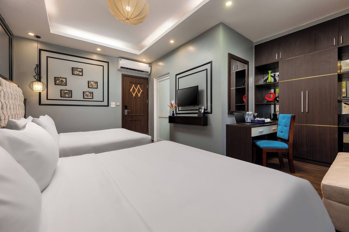 A hotel room with two beds, a desk with a chair, a TV mounted on the wall, and a wardrobe.